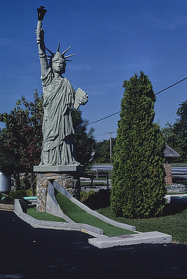 A rudimentary replica of the Statue of Liberty is positioned over one of the putting areas at a miniature golf course.
