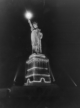 Spotlights point up at the Statue of Liberty, whose torch is illuminated and whose pedestal is strung with lights.